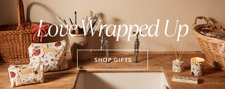 Collection of lifestyle gifting products, including a candle, diffuser, pillow spray, wash bag and cosmetic bag in our cream pressed floral print. Copy on image 'Love Wrapped Up - Shop Gifts'