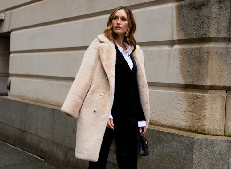 Image showing model wearing the Sienna Tailored Velvet Blazer In black with Sienna Straight Leg Velvet Trouser In Black. The Emma Longline Faux Fur Coat In cream is draped over her shoulder.